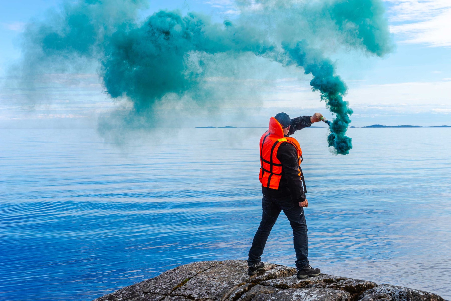 man wearing lifejacket with blue smoke signal in distress